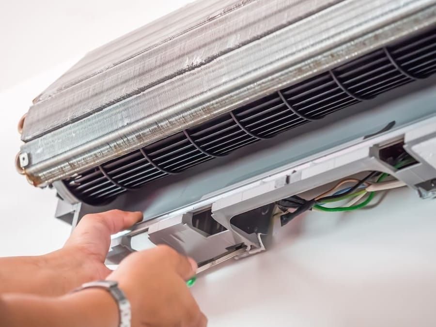 Technician servicing energy-efficient ductless air conditioner indoor unit.