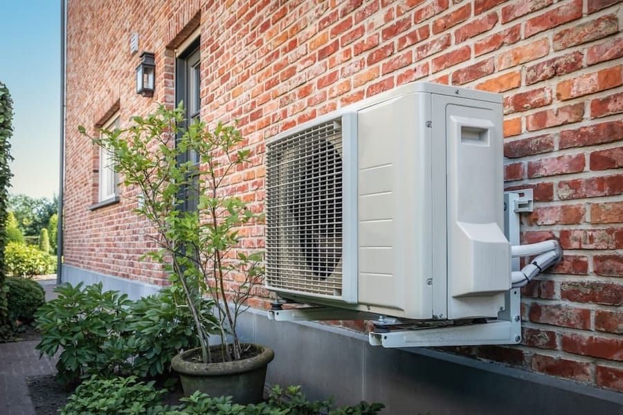 Outdoor residential heat pump unit installed beside brick home for heating and cooling services.