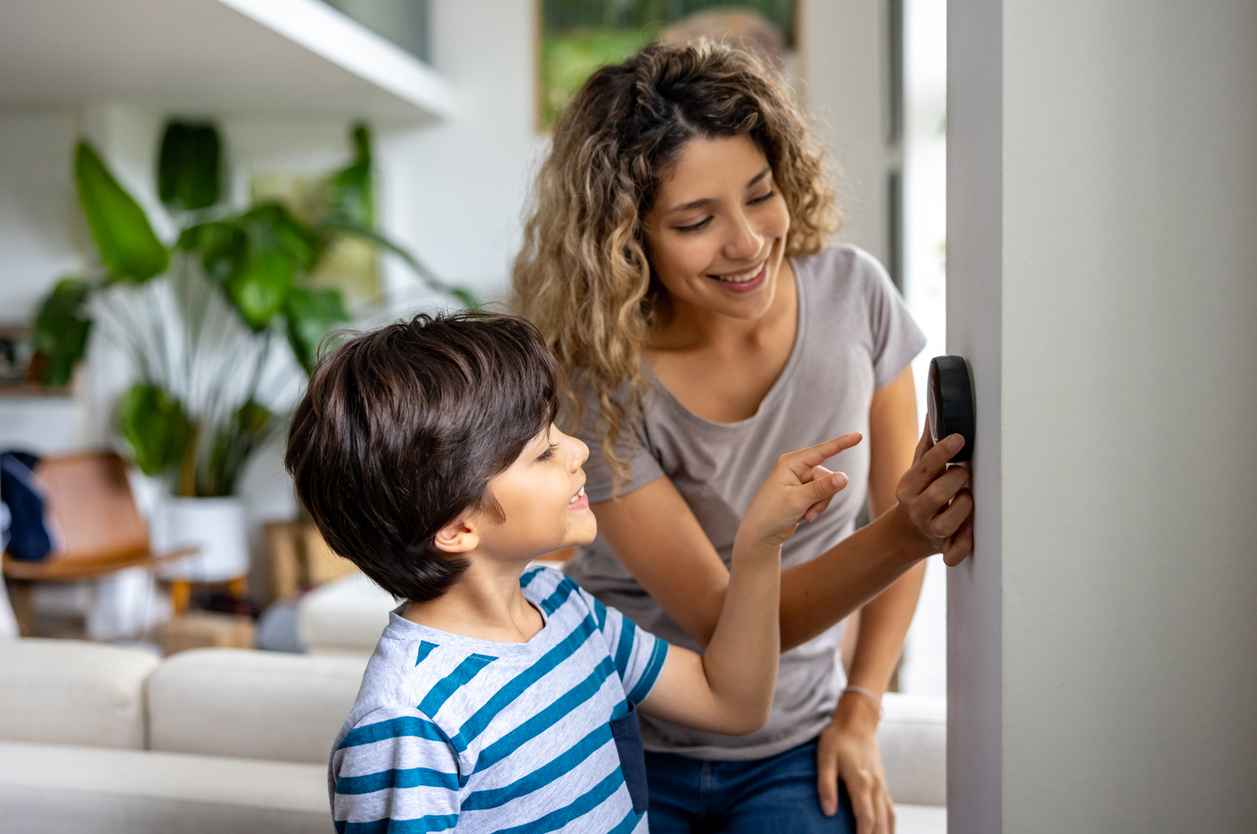 A mother with her young son checking their thermostat in the house