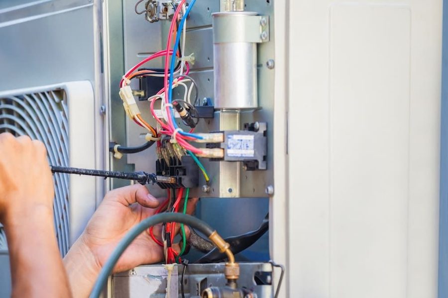 HVAC technician repairing an HVAC system with wires to the unit showing
